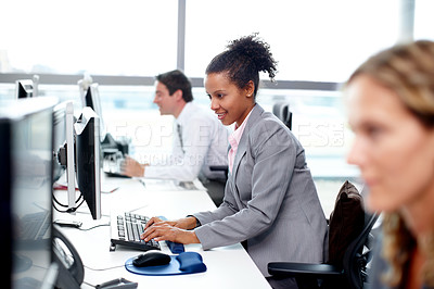 Buy stock photo Young businesswoman working on her computer with her colleagues around her 