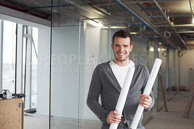 Buy stock photo Young architect standing in a building and holding his plans with a smile