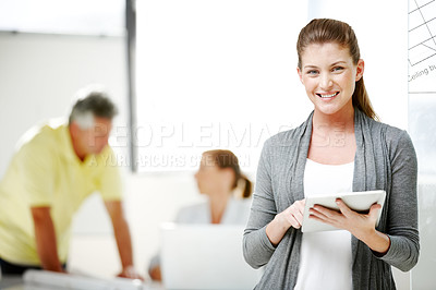 Buy stock photo A young female architect standing and using a digital tablet with her co-workers in the background