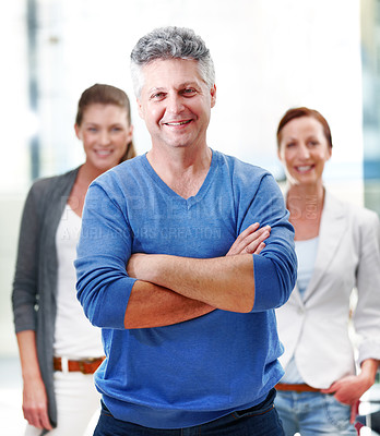 Buy stock photo Portrait of a mature businessman standing confidently with his co-workers behind him