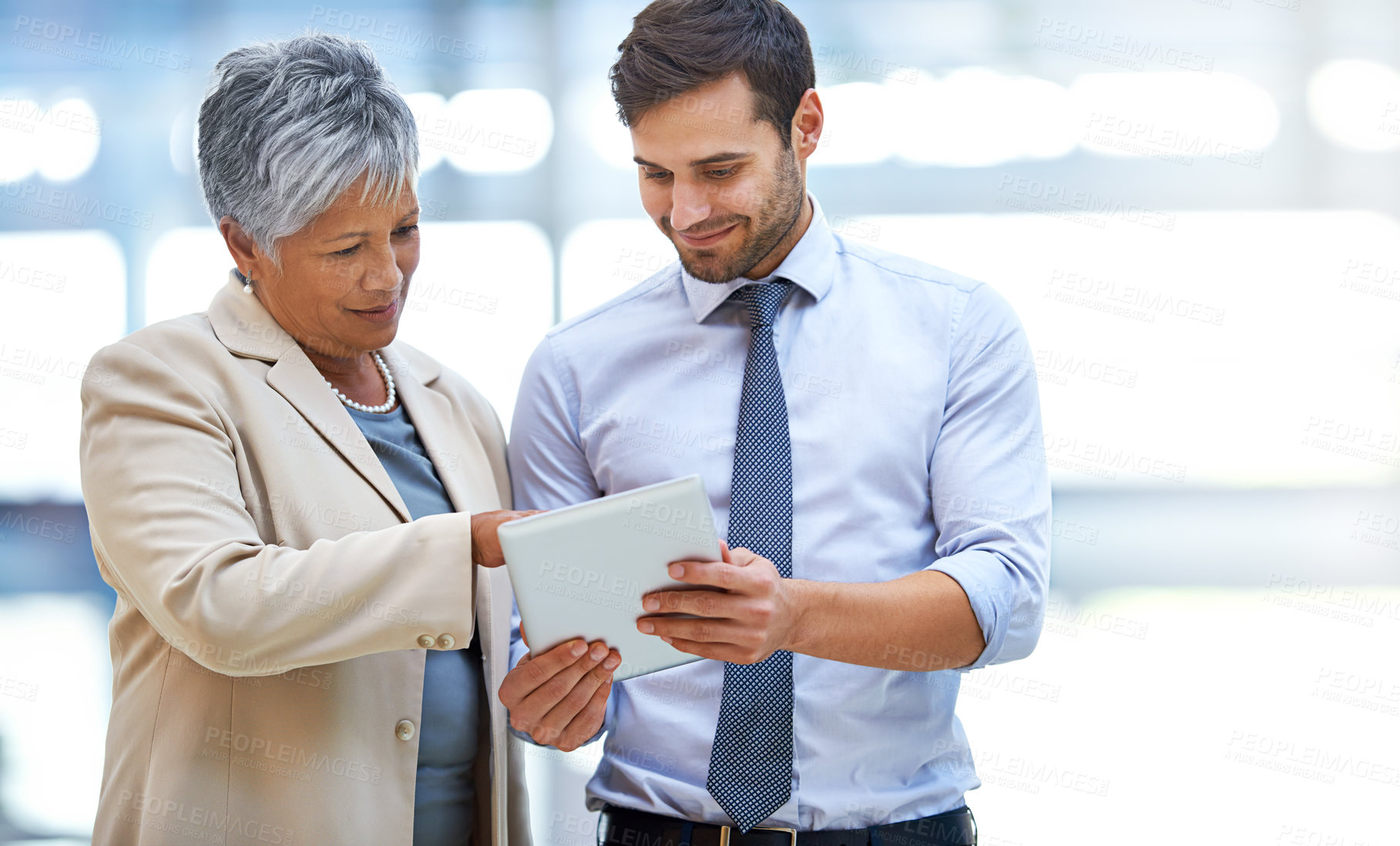 Buy stock photo Shot of two business colleagues discussing work while standing with a digital tablet
