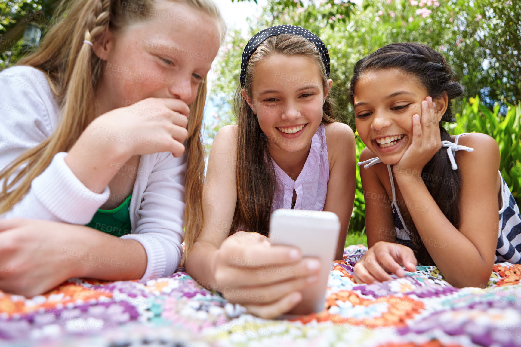 Buy stock photo A young girl showing her friends something on a cellphone while they're relaxing outside