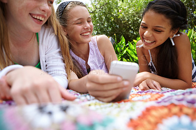 Buy stock photo Shot of a group of young girls chatting while relaxing outside with a cellphone