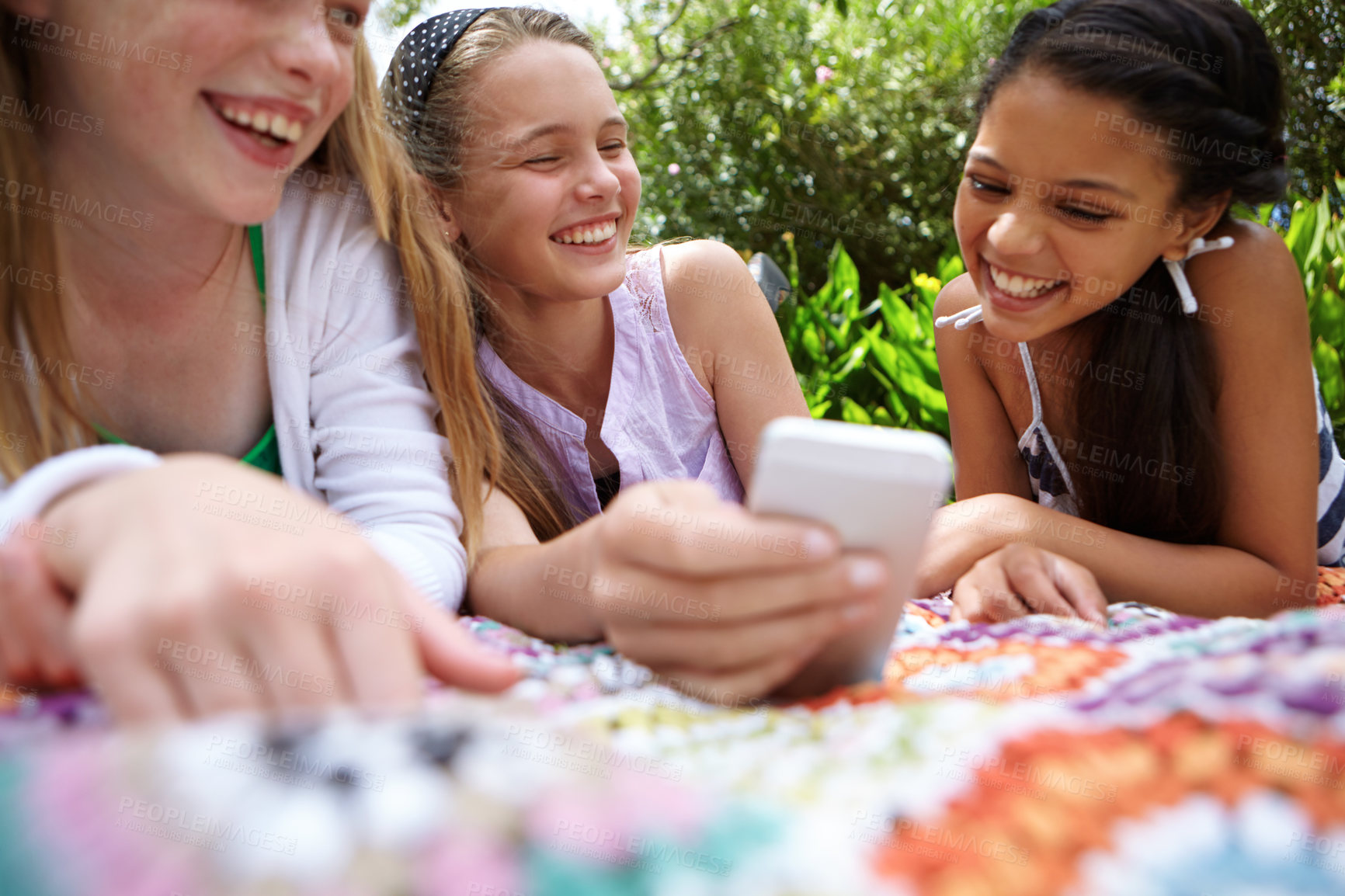 Buy stock photo Shot of a group of young girls chatting while relaxing outside with a cellphone