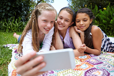 Buy stock photo Shot of a group of young girls taking a selfie together while lying on a blanket outside