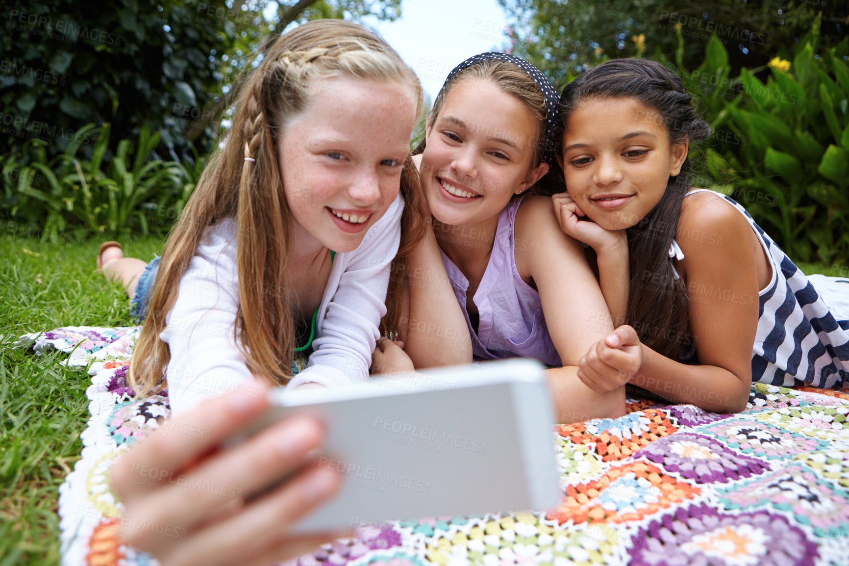 Buy stock photo Shot of a group of young girls taking a selfie together while lying on a blanket outside