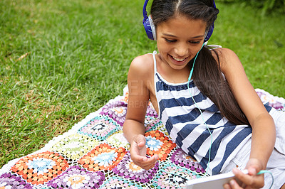 Buy stock photo Shot of a young girl listening to music on her cellphone while relaxing outside