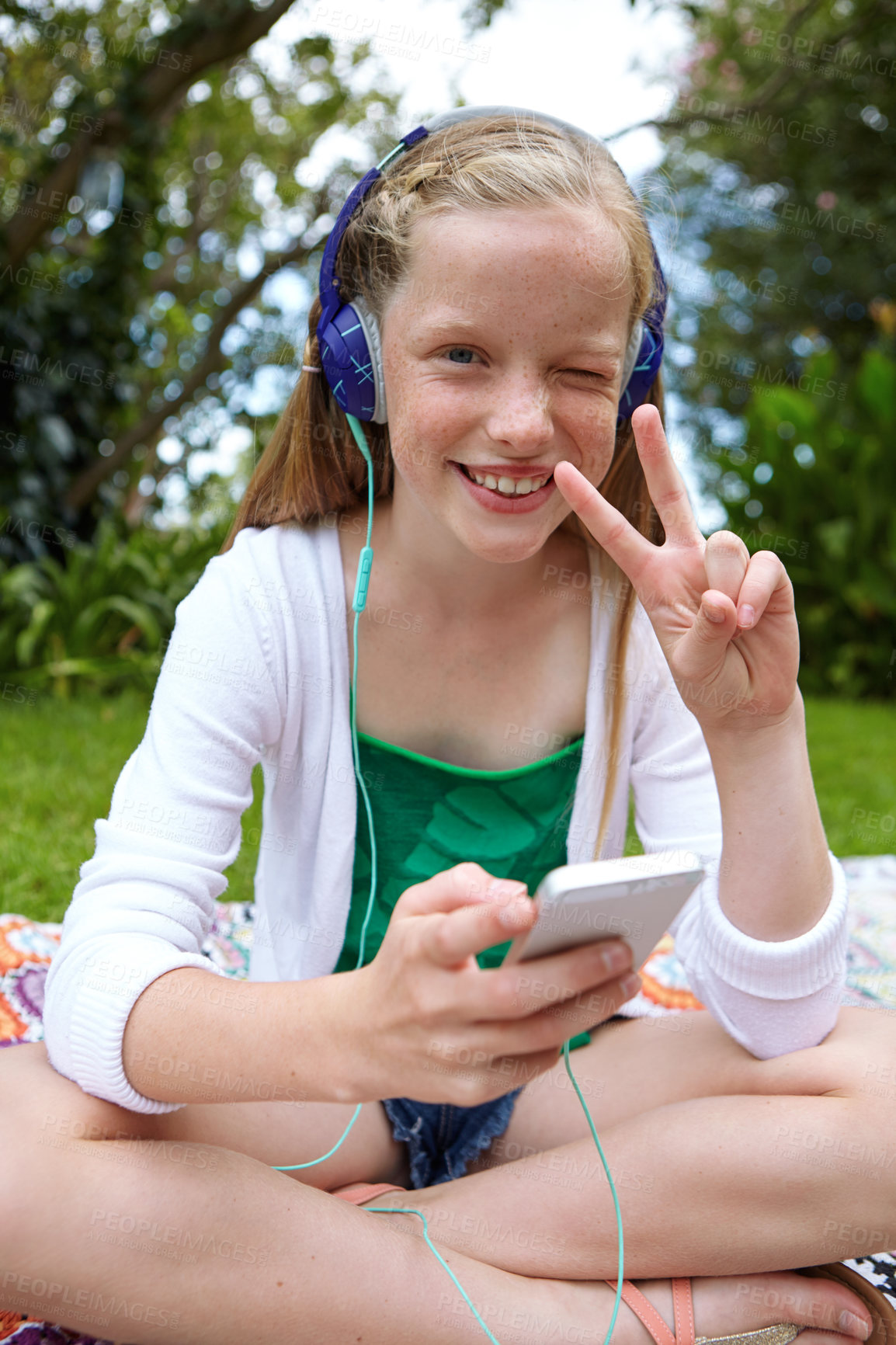 Buy stock photo Shot of a young girl listening to music on her cellphone while sitting outside