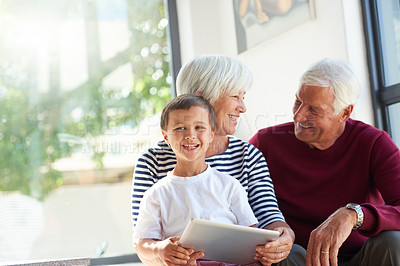 Buy stock photo Shot of a little boy holding a tablet while sitting with his grandparents