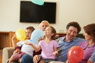 Buy stock photo Shot of a brother and sister playing with balloons while sitting with their family