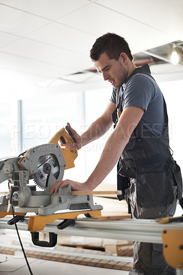 Buy stock photo Young contractor using a saw while on a construction site 