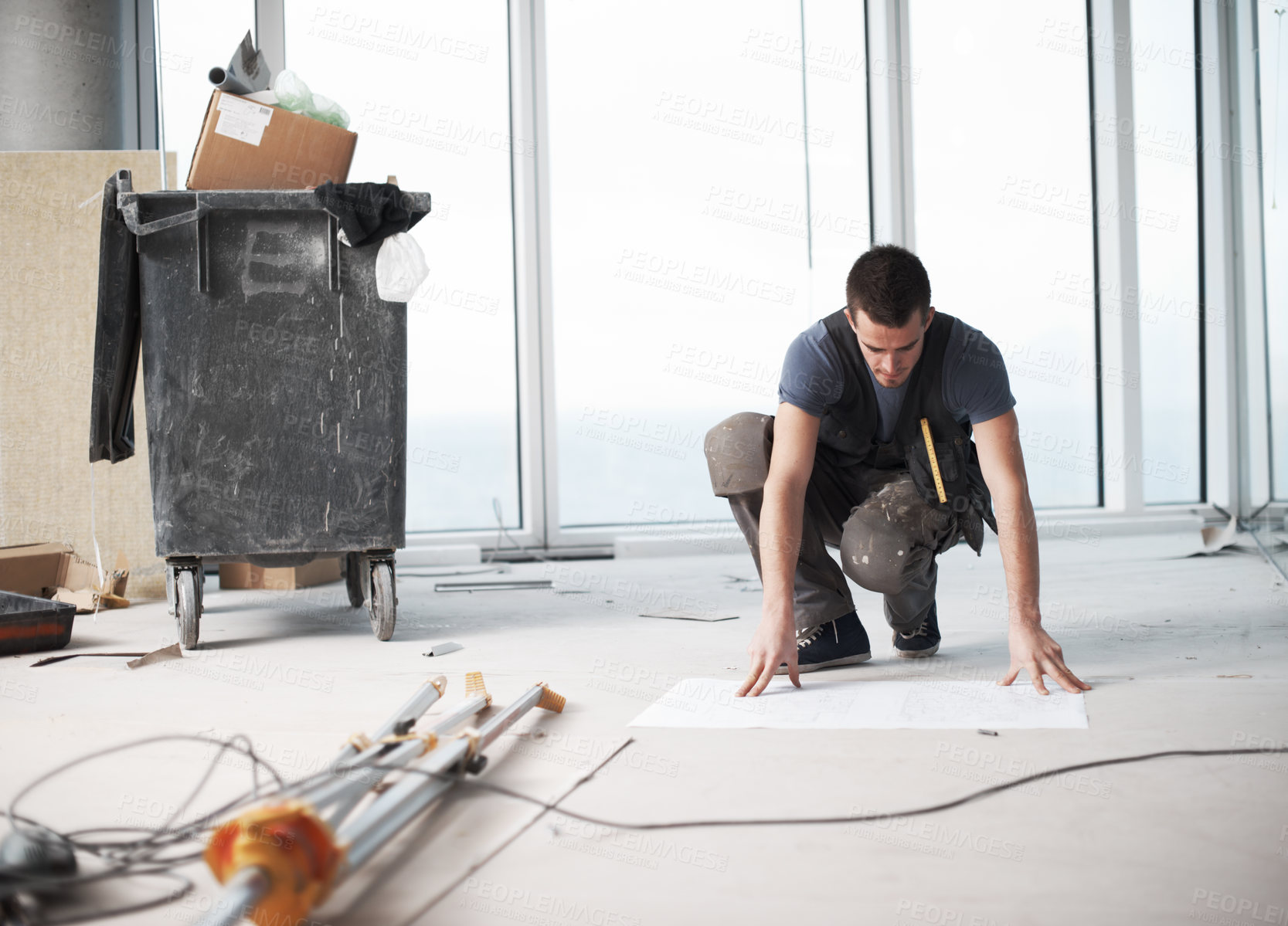 Buy stock photo A contractor checking his plans on a construction site. Professional in overalls with the floorplan. A male cabling contractor working on the new building and checking on his blueprint.