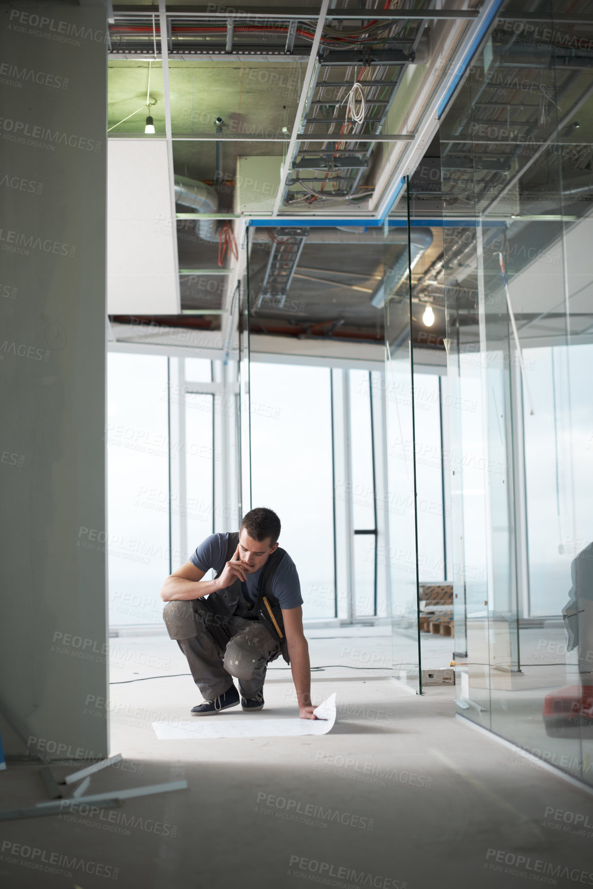 Buy stock photo Young contractor checking his plans on a construction site indoors