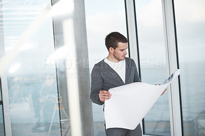 Buy stock photo Young architect checking his plans while standing in an empty room