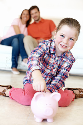 Buy stock photo A young girl puts money in a piggybank while her parents watch