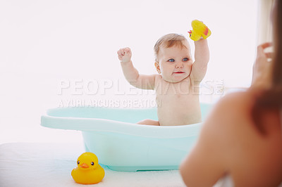 Buy stock photo A baby girl playing with her toys in the bathtub while her mom stands by