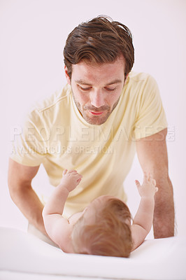 Buy stock photo A father showing affection to his baby daughter as she lies on a changing table