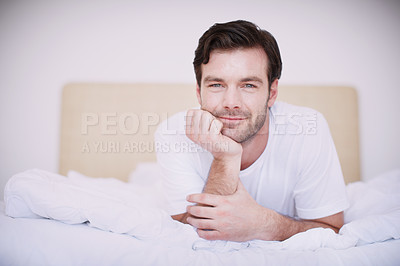 Buy stock photo Shot of a handsome young man lying on his stomach on a bed