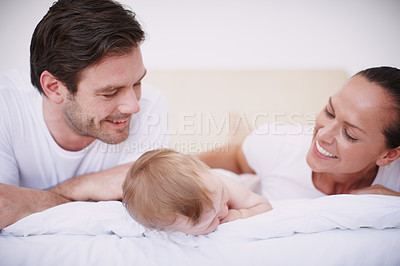Buy stock photo Two loving young parents and their adorable baby girl lying together on a bed