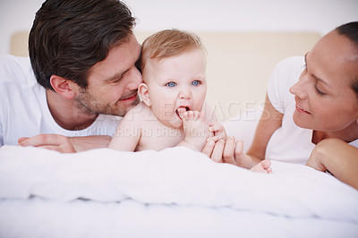 Buy stock photo Two loving young parents and their adorable baby daughter lying together on a bed