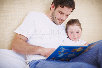 Buy stock photo A devoted father reading his young daughter a bedtime story