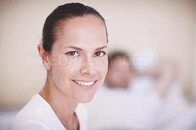 Buy stock photo Portrait of an attractive young woman in a bedroom with her husband lying in the background