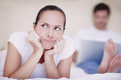 Buy stock photo A young woman looking annoyed with her husband who is sitting in the background with a laptop