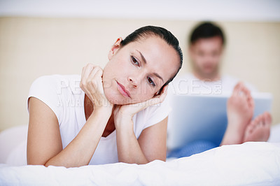 Buy stock photo A young woman looking bored while her husband sits with his laptop in the background