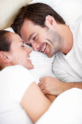 Buy stock photo Portrait of a young couple lying in bed and laughing
