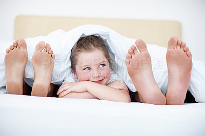 Buy stock photo Fun shot of a young girl peeking out from between her parents feet while they lie in bed