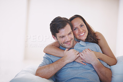 Buy stock photo A loving young wife hugging her husband from behind while he sits on a sofa