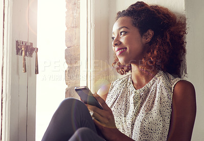 Buy stock photo Shot of a young woman using her cellphone while sitting by a window