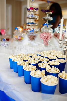 Buy stock photo Popcorn in paper cups on a table at a wedding reception. Delicious butter popcorn in disposable blue cups arranged in a row on a sweets and treats snacking table at a birthday party