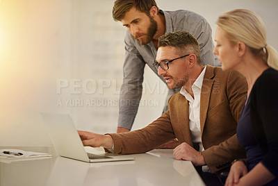 Buy stock photo Cropped shot of three businesspeople looking at a laptop in the boardroom