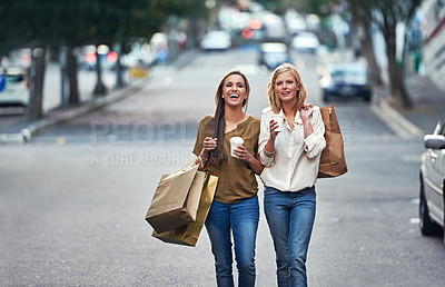 Buy stock photo Shot of two young women walking down a street carrying shopping bags