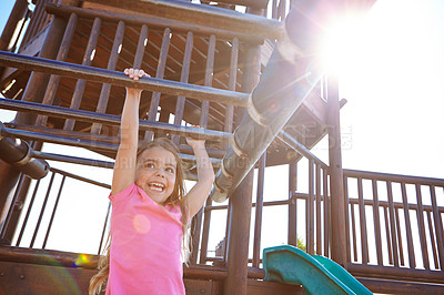 Buy stock photo Shot of a little girl hanging on the monkey bars at the playground