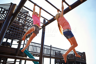 Buy stock photo Shot of two little girls hanging on the monkey bars at the playground