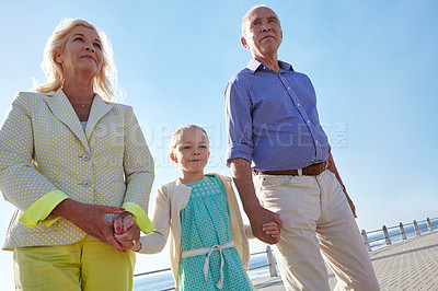 Buy stock photo Shot of grandparents walking hand in hand with their granddaughter on a promanade