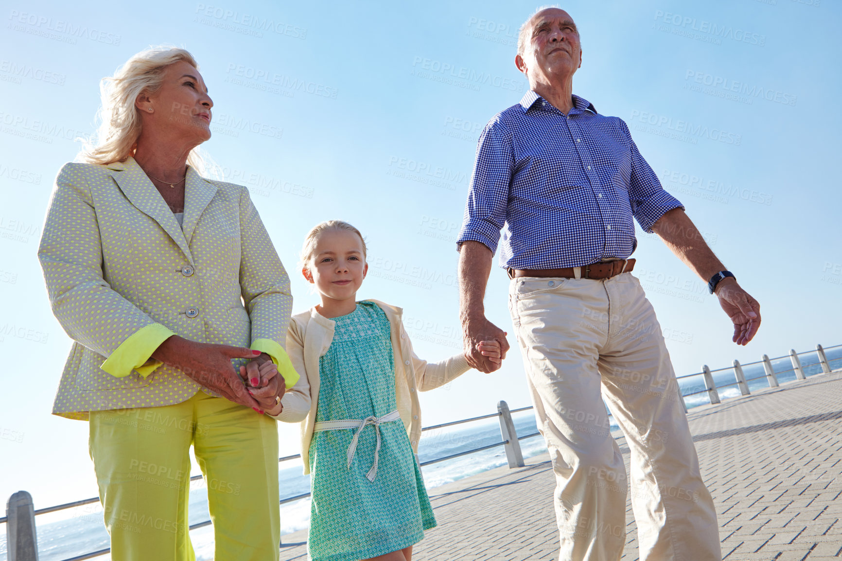 Buy stock photo Shot of grandparents walking hand in hand with their granddaughter on a promanade