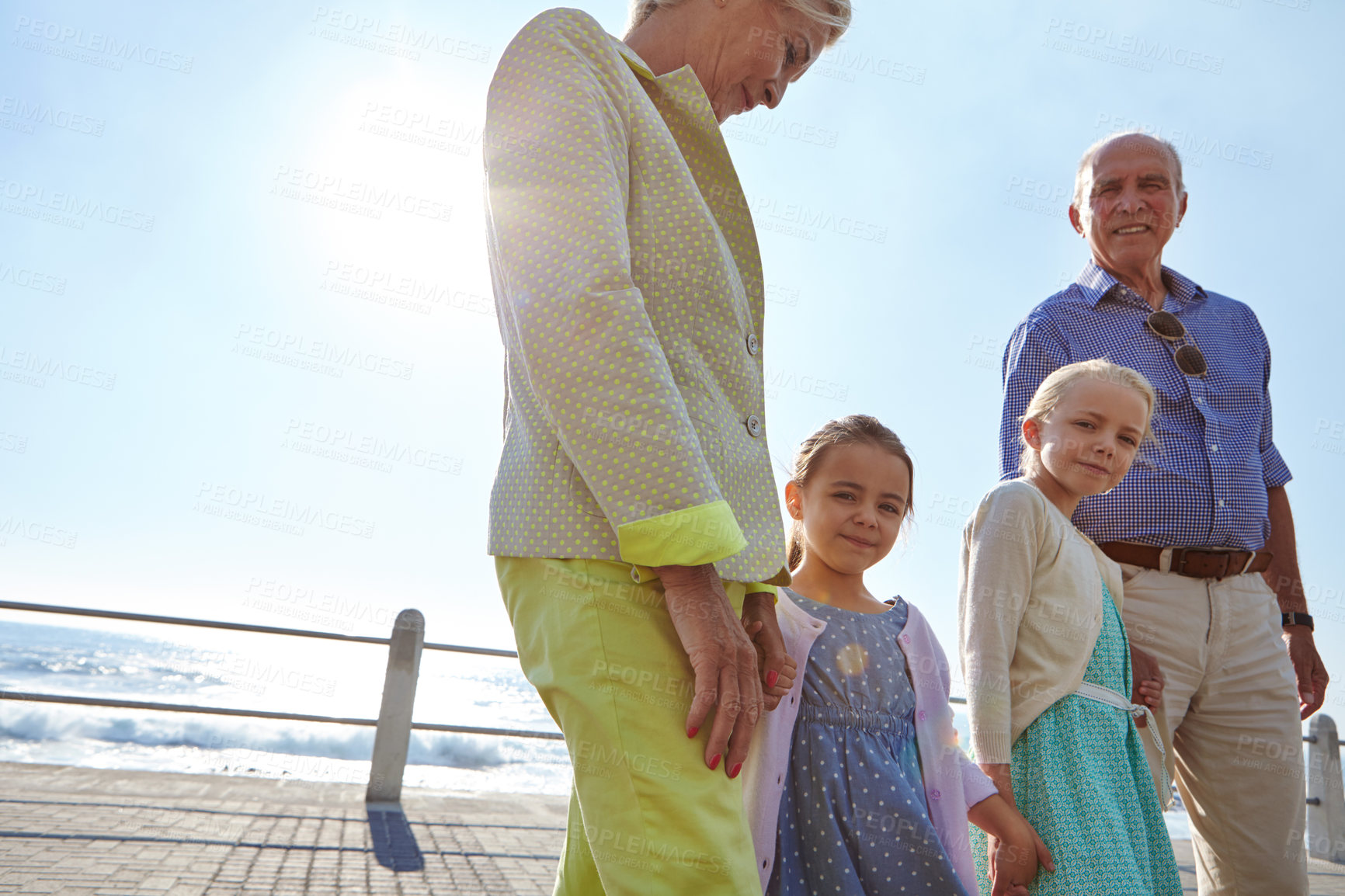 Buy stock photo Shot of grandparents walking hand in hand with their granddaughters on a promanade