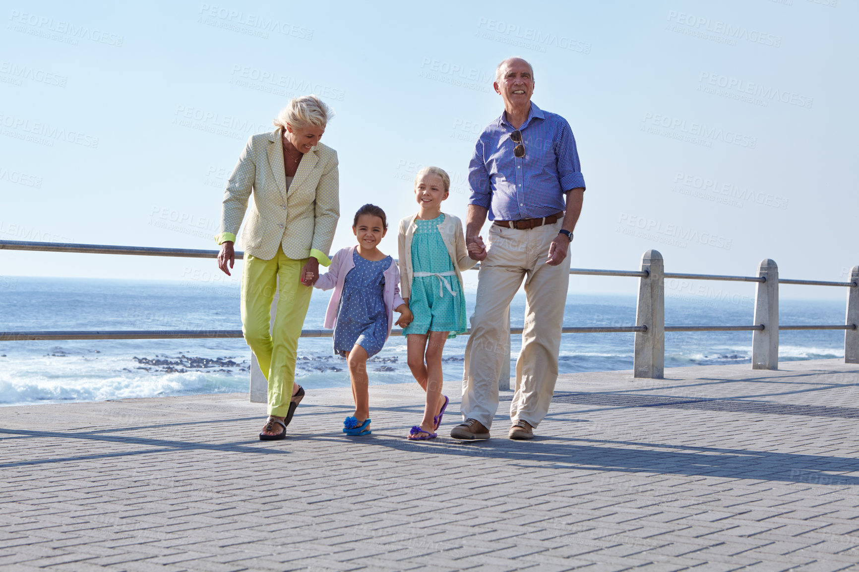 Buy stock photo Shot of grandparents walking hand in hand with their granddaughters on a promanade