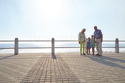 Buy stock photo Shot of grandparents walking hand in hand with their granddaughters on a promanade