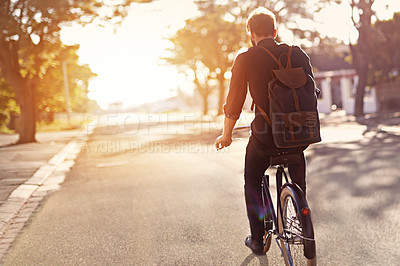 Buy stock photo Rearview shot of a young man riding a bicycle outdoors