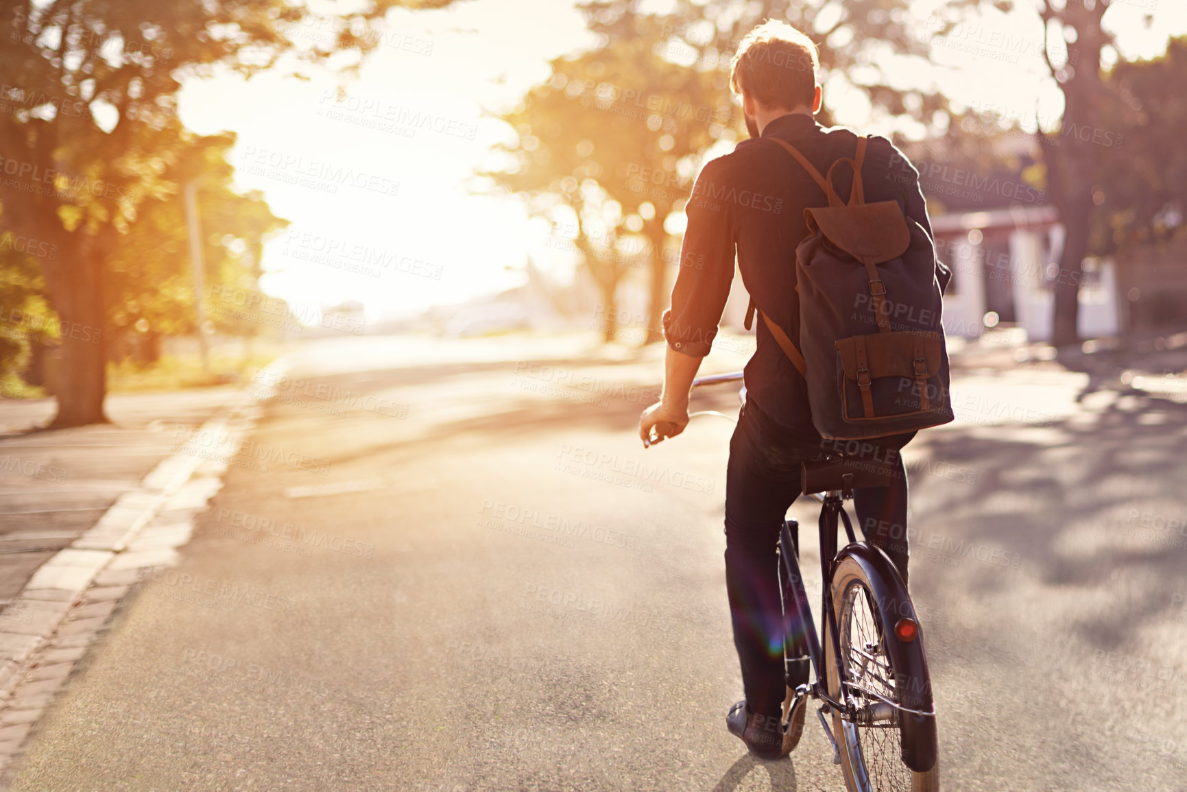 Buy stock photo Rearview shot of a young man riding a bicycle outdoors