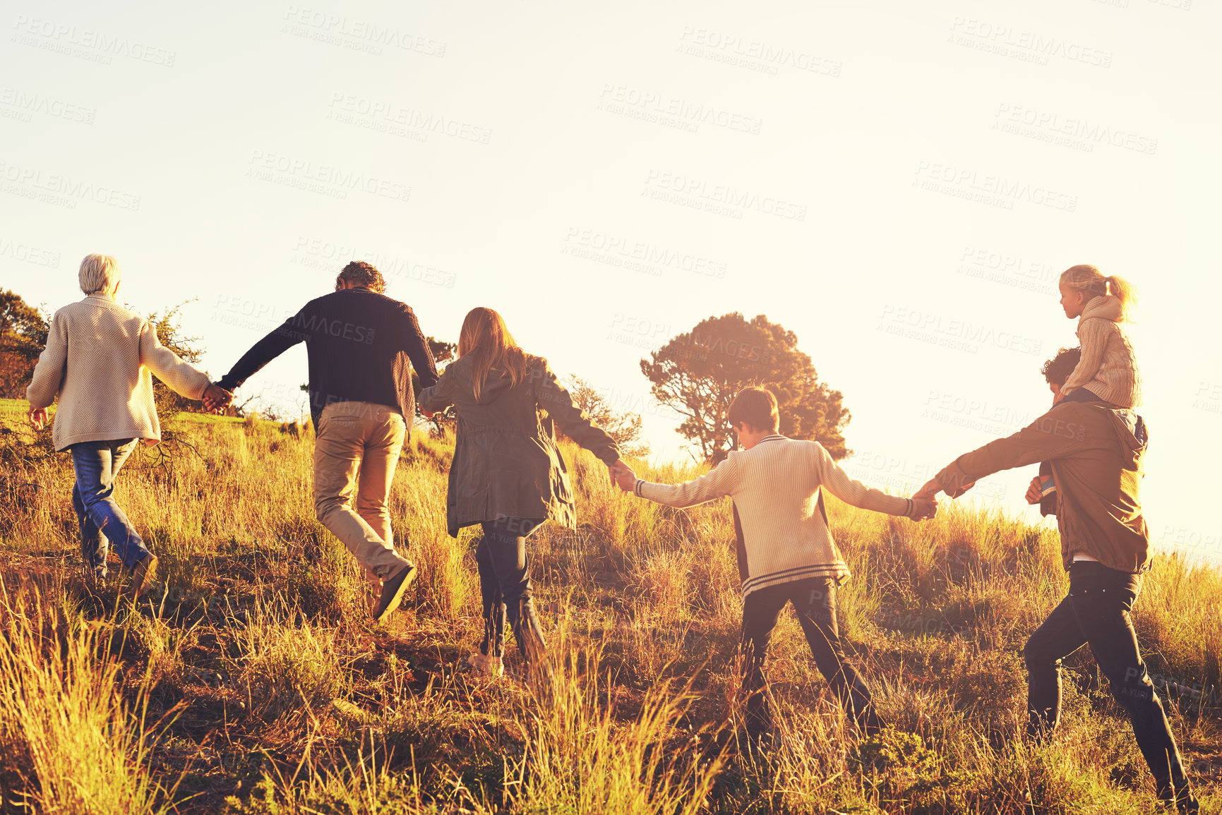Buy stock photo A multi-generational family walking up a grassy hill together at sunse