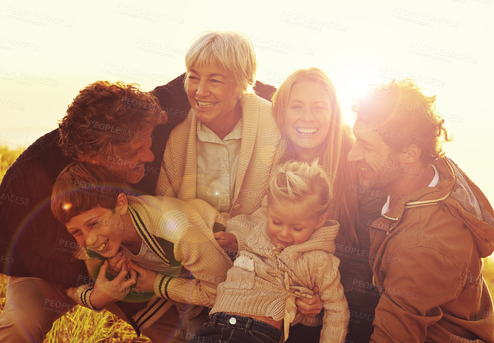 Buy stock photo Happy, love and big family in nature at sunset hugging, bonding and spending quality time together. Happiness, smile and children posing with their parents and grandparents in outdoor field at dusk.