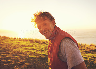 Buy stock photo Sunset, nature and portrait of man by ocean for adventure, relaxing and enjoy weekend outdoors. Happy, smile and person with flare on hill for holiday, vacation and travel destination in evening
