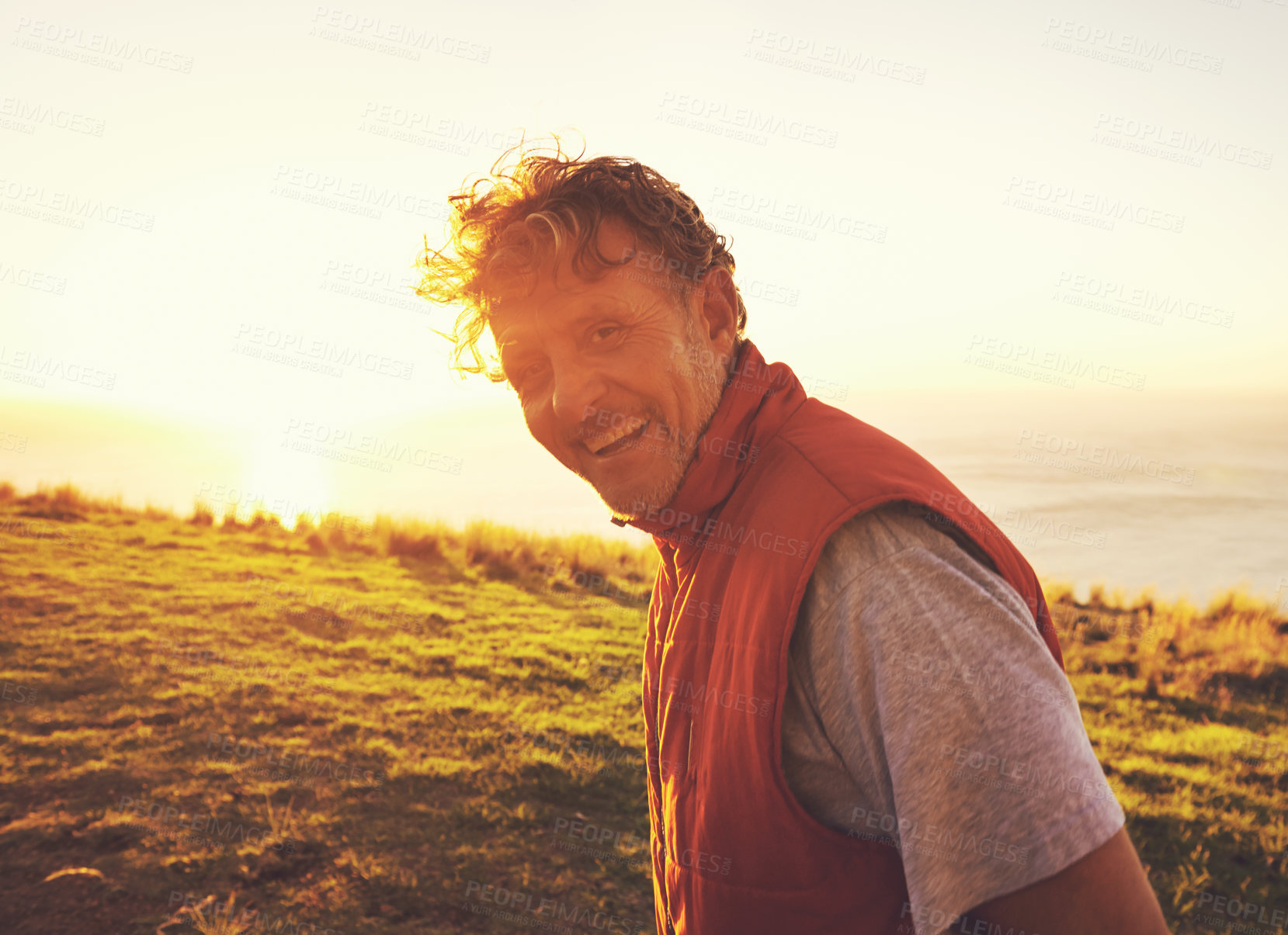 Buy stock photo Sunset, nature and portrait of man by ocean for adventure, relaxing and enjoy weekend outdoors. Happy, smile and person with flare on hill for holiday, vacation and travel destination in evening