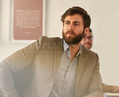 Buy stock photo Shot of a young businessman sitting in his office with his colleague blurred in the background