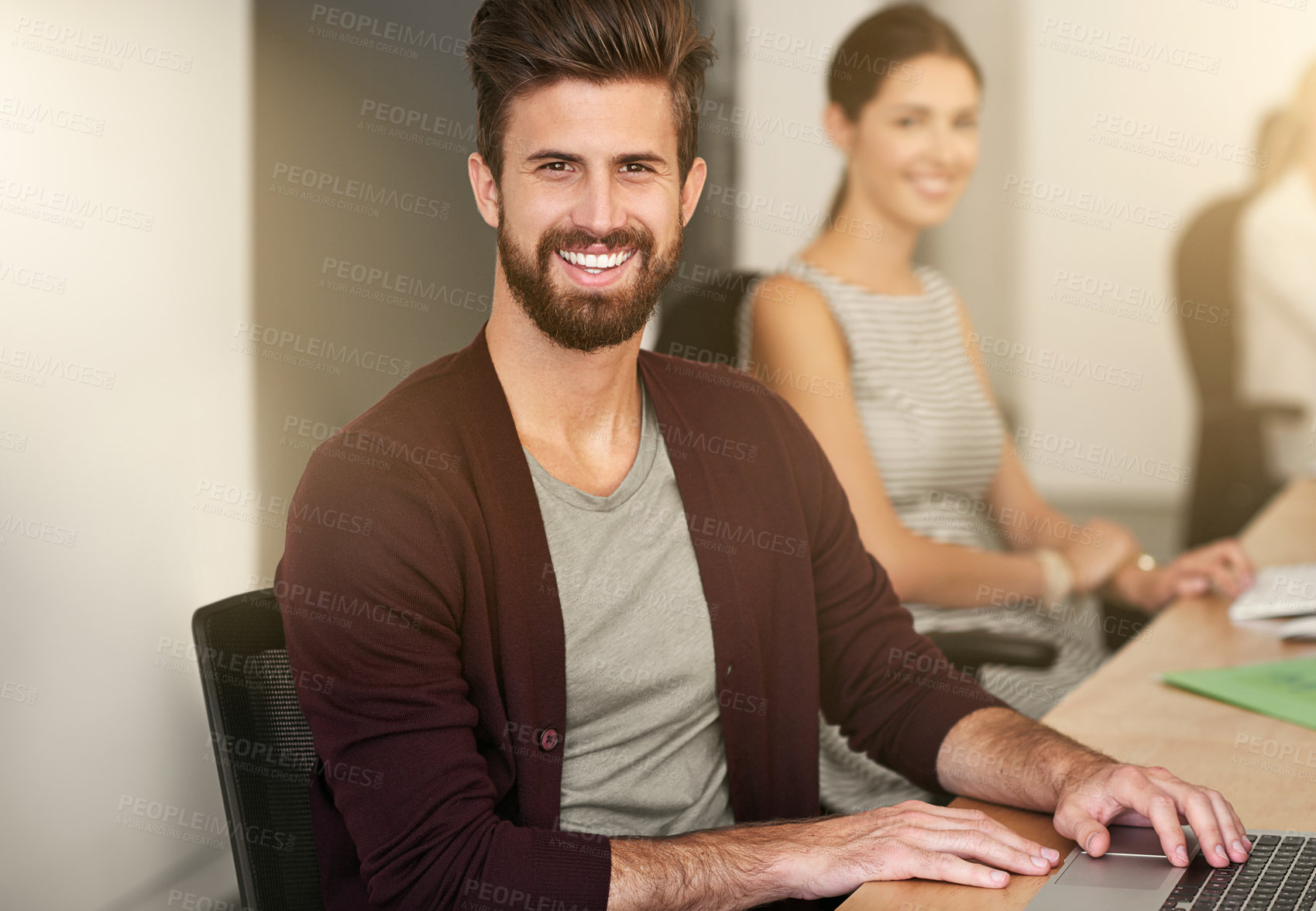 Buy stock photo Portrait of a young designer sitting in an office with his colleague blurred in the background